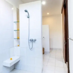 Asraya villa brightly lit guest bathroom shower stall featuring crisp white tiles a handheld fixture recessed glass shelves and a seat sanur 870x500