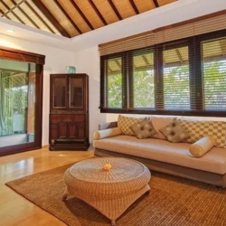 Asraya villa comfortable master bedroom sitting area featuring a thatched ceiling wooden flooring stylish sofa and woven coffee table sanur 870x500